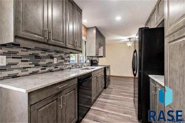 kitchen featuring black appliances, a sink, backsplash, light wood finished floors, and baseboards