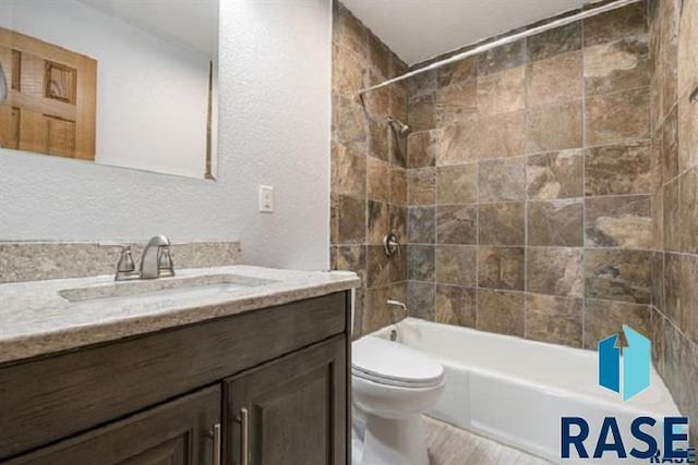 bathroom with toilet, vanity, washtub / shower combination, wood finished floors, and a textured wall