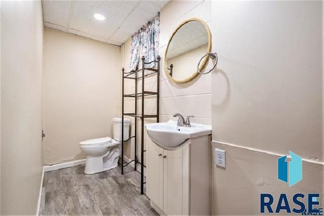 bathroom featuring wood finished floors, toilet, vanity, and a paneled ceiling