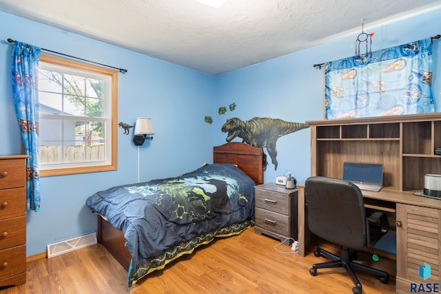 bedroom with wood finished floors, a textured ceiling, baseboards, and a desk