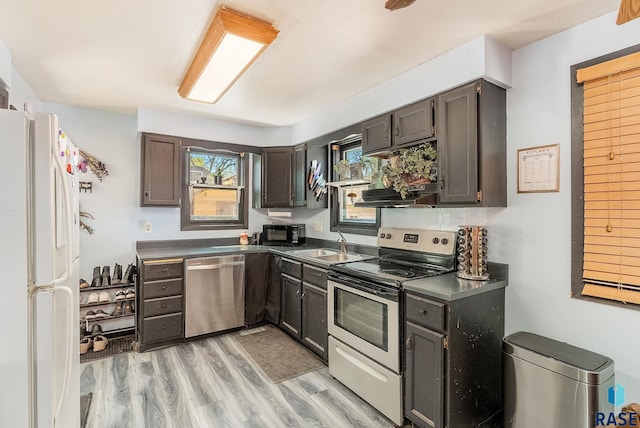 kitchen with appliances with stainless steel finishes, dark countertops, a sink, and light wood-style flooring