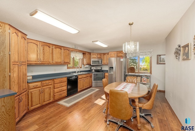 kitchen with appliances with stainless steel finishes, a sink, light wood-style floors, a chandelier, and brown cabinets