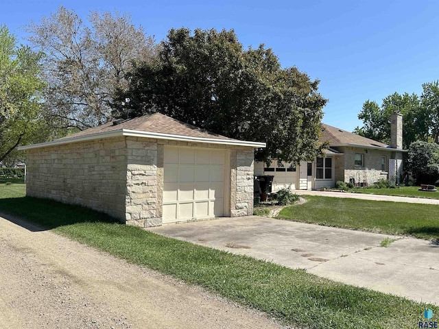 view of front of property featuring concrete driveway, stone siding, a front lawn, a chimney, and an outbuilding