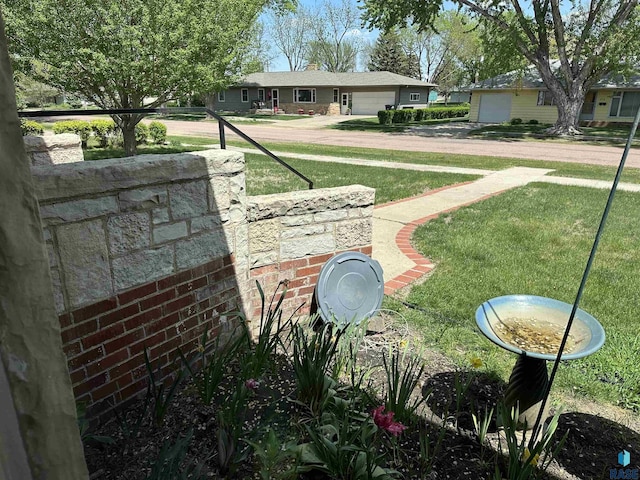 view of green lawn with an attached garage and driveway