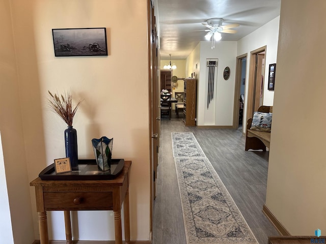 hall featuring a chandelier, wood finished floors, and baseboards