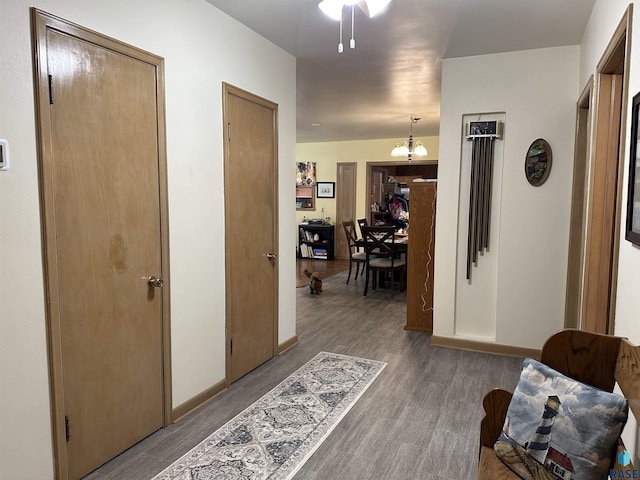corridor featuring wood finished floors, a chandelier, and baseboards