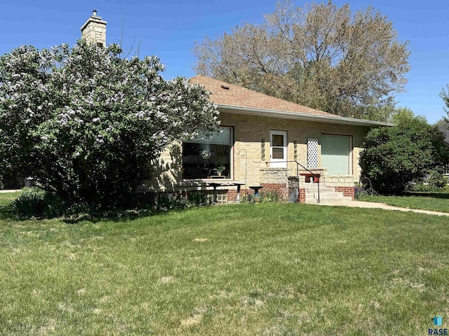 rear view of house with entry steps, a yard, and roof with shingles