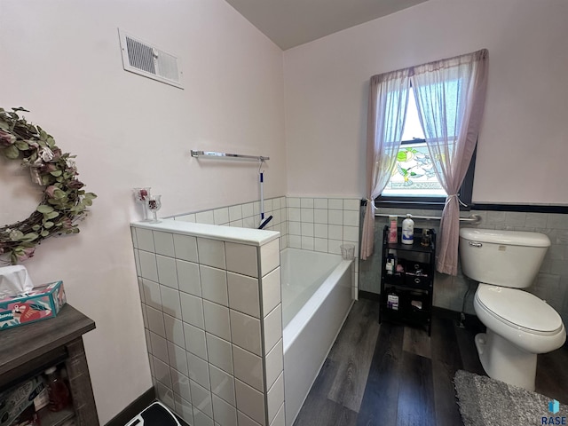 full bath with wood finished floors, tile walls, a wainscoted wall, toilet, and a bath