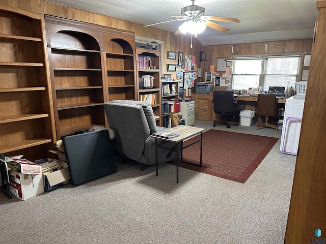 carpeted home office featuring wood walls and ceiling fan