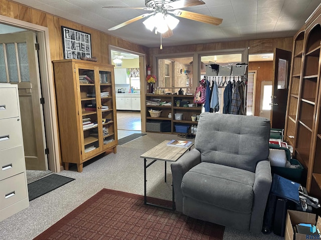 living area featuring wooden walls, a ceiling fan, and carpet