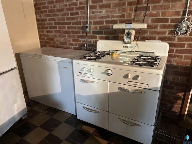 kitchen featuring white appliances, brick wall, dark floors, and washer / dryer