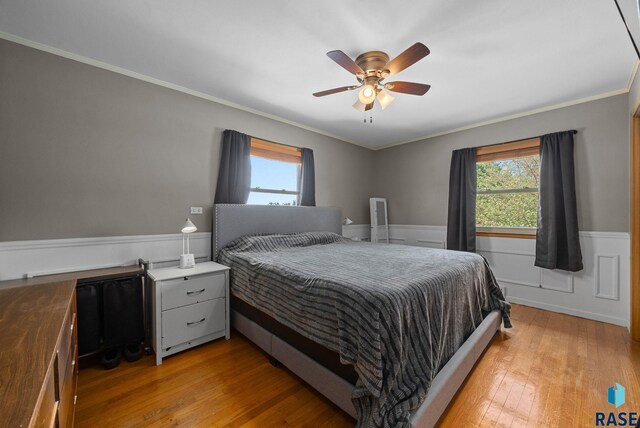 bedroom with a wainscoted wall, light wood-type flooring, ornamental molding, and ceiling fan