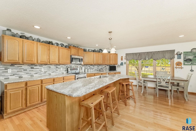 kitchen with appliances with stainless steel finishes, light wood-type flooring, backsplash, a kitchen breakfast bar, and a textured ceiling