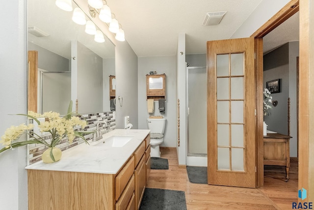 full bath with wood finished floors, decorative backsplash, a shower stall, vanity, and toilet