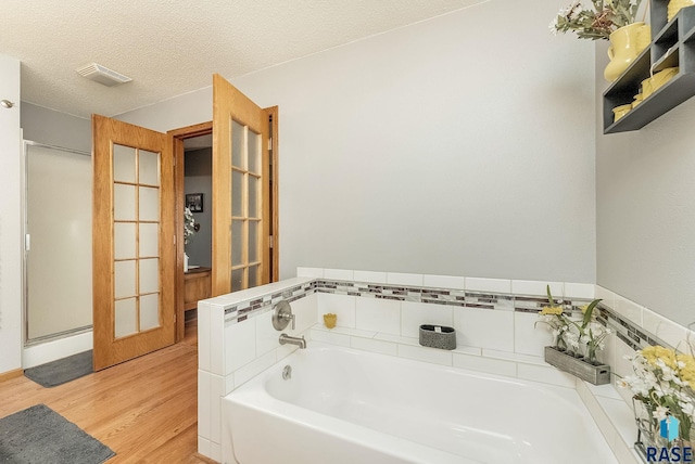 bathroom featuring wood finished floors, a garden tub, french doors, a stall shower, and a textured ceiling