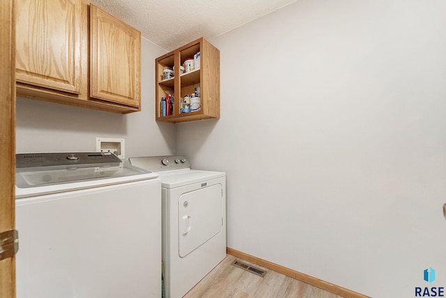 washroom with cabinet space, independent washer and dryer, light wood-style flooring, baseboards, and a textured ceiling