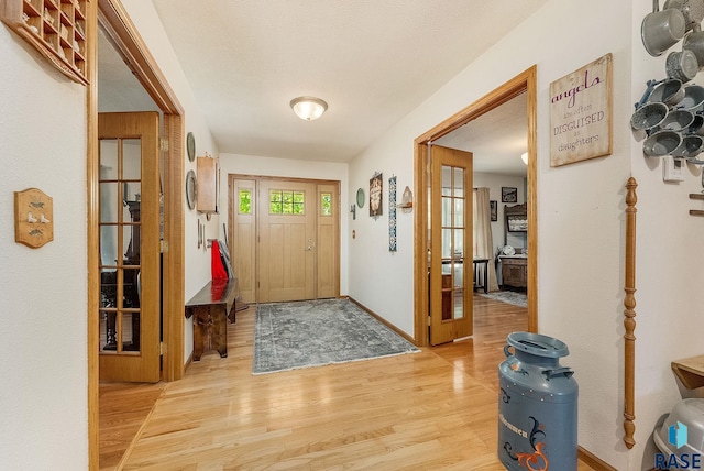 entryway with light wood finished floors, french doors, and baseboards
