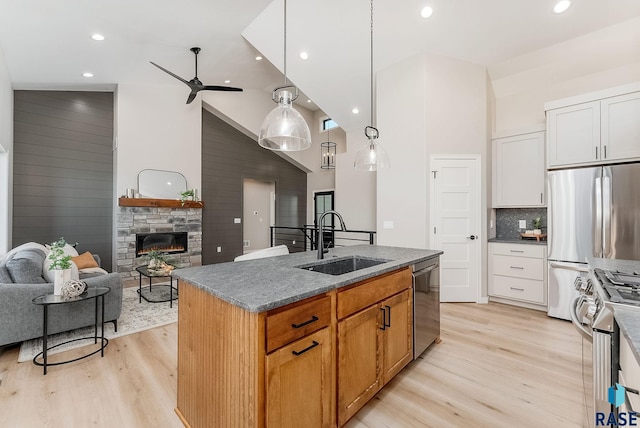 kitchen with a sink, appliances with stainless steel finishes, light wood-style flooring, high vaulted ceiling, and a stone fireplace