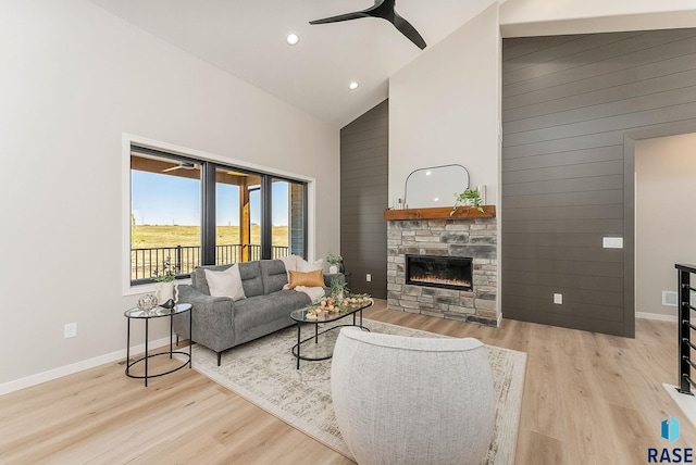 living area with high vaulted ceiling, a stone fireplace, light wood-style floors, baseboards, and recessed lighting