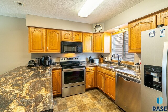 1805 S Sertoma Ave Unit 105, Sioux Falls, SD 57106 - kitchen with appliances with stainless steel finishes, a sink, dark countertops, brown cabinetry, and a textured ceiling