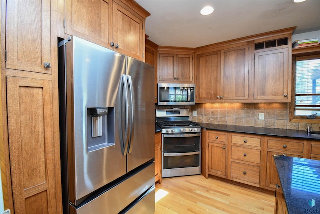 4600 S Harrington Ave, Sioux Falls, SD 57103 - kitchen featuring appliances with stainless steel finishes, dark countertops, light wood-style flooring, brown cabinets, and tasteful backsplash