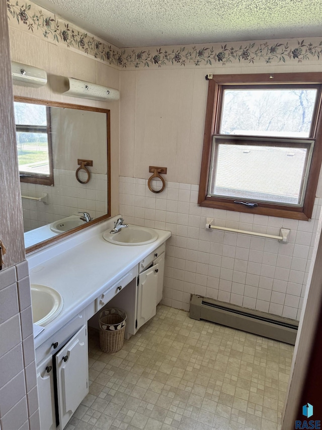 bathroom featuring baseboard heating, plenty of natural light, tile walls, double vanity, and a textured ceiling