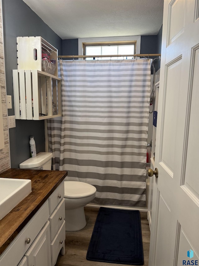 bathroom with wood finished floors, vanity, toilet, curtained shower, and a textured ceiling