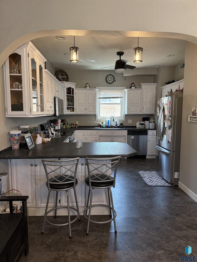 kitchen featuring stainless steel appliances, a peninsula, a sink, dark countertops, and white cabinets
