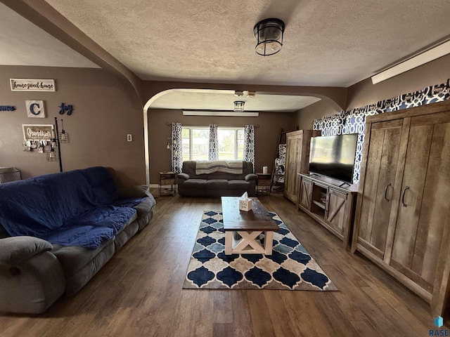 living room with arched walkways, dark wood-style flooring, and a textured ceiling