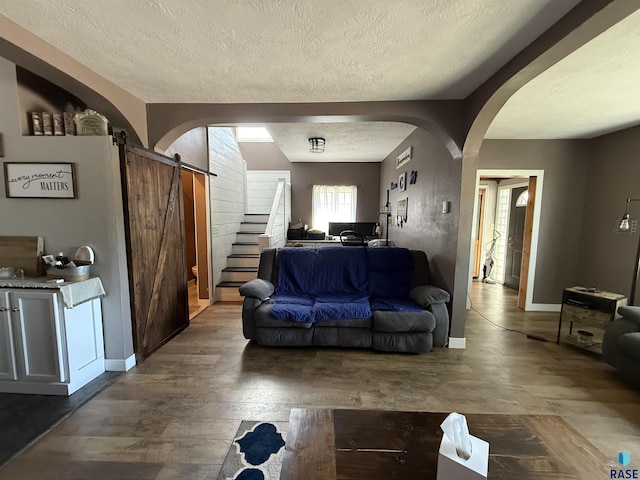 living room with a barn door, arched walkways, a textured ceiling, wood finished floors, and baseboards
