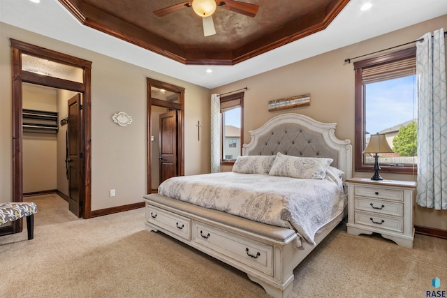 bedroom featuring a tray ceiling, light carpet, baseboards, a walk in closet, and recessed lighting