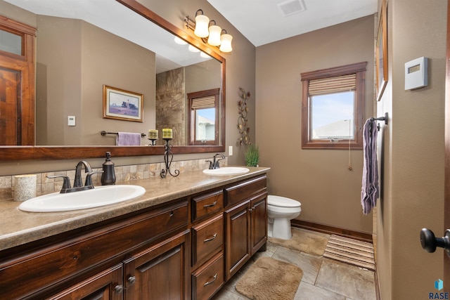 full bath with toilet, double vanity, and baseboards