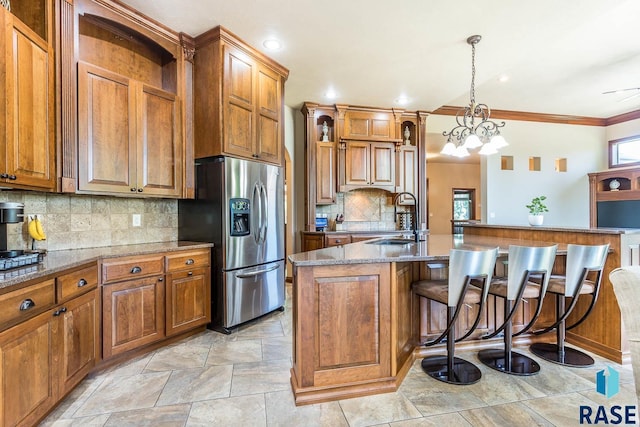 kitchen with stainless steel refrigerator with ice dispenser, a sink, brown cabinetry, a kitchen bar, and backsplash