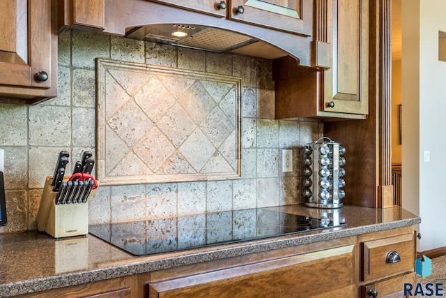 kitchen with black electric cooktop, brown cabinetry, backsplash, and arched walkways