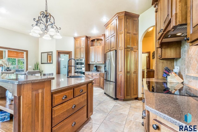 kitchen featuring appliances with stainless steel finishes, decorative backsplash, arched walkways, brown cabinets, and pendant lighting