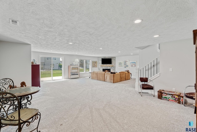 carpeted living room featuring a textured ceiling, a stone fireplace, recessed lighting, and stairway