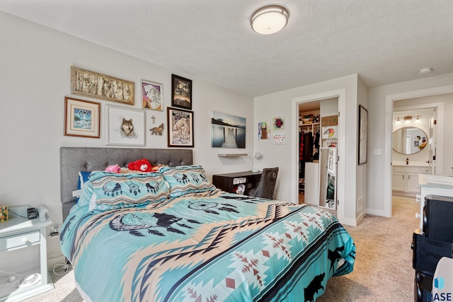 bedroom with light colored carpet, a walk in closet, a closet, a textured ceiling, and connected bathroom