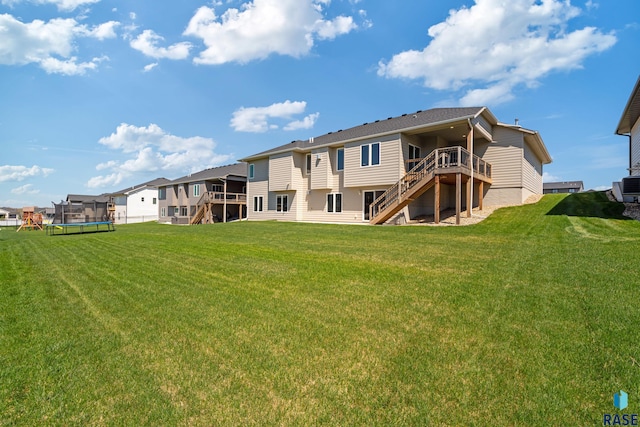 back of house featuring stairway, a trampoline, a wooden deck, and a lawn