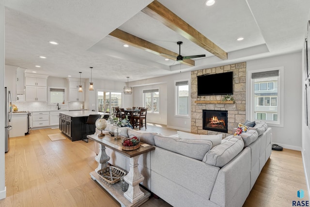 living room with light wood finished floors, ceiling fan, baseboards, a stone fireplace, and recessed lighting