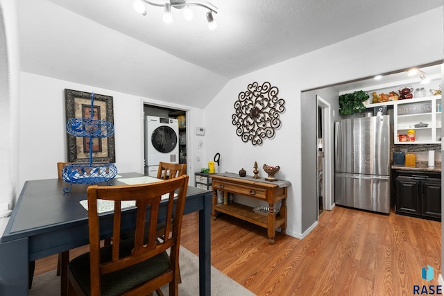 dining room featuring stacked washer / dryer, lofted ceiling, and light wood-style floors