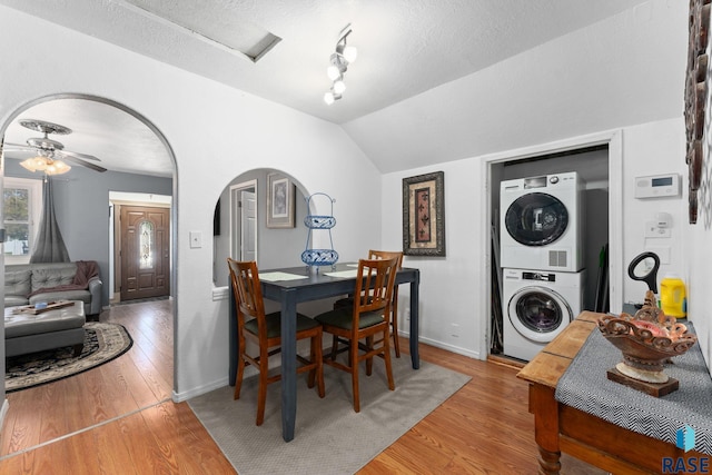 dining area featuring stacked washer and clothes dryer, arched walkways, light wood-style flooring, a ceiling fan, and baseboards