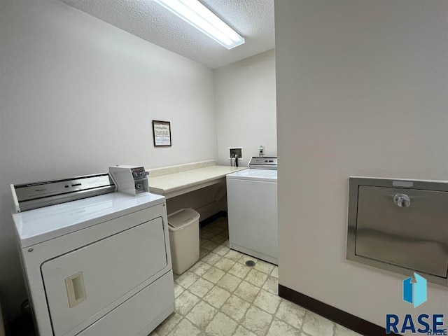laundry room featuring washing machine and clothes dryer, a textured ceiling, baseboards, and light floors