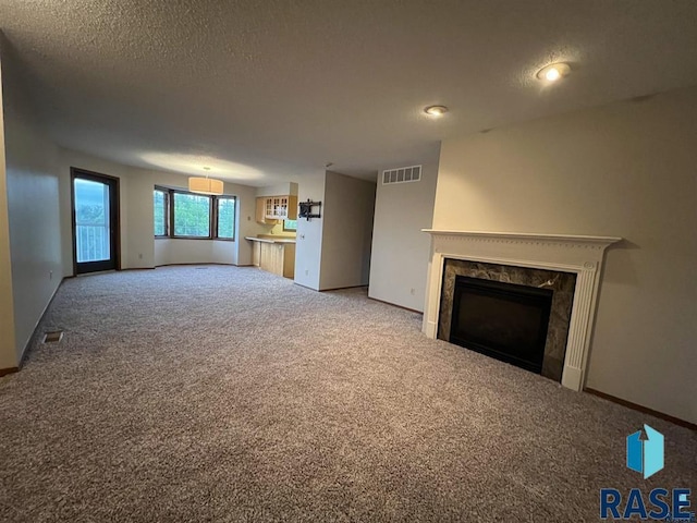 unfurnished living room with carpet, a high end fireplace, baseboards, and a textured ceiling