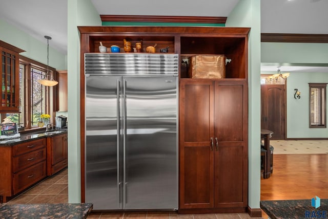 kitchen with stainless steel built in fridge, open shelves, decorative light fixtures, dark stone countertops, and glass insert cabinets