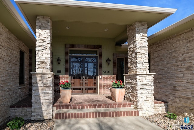 view of exterior entry with covered porch, french doors, and brick siding