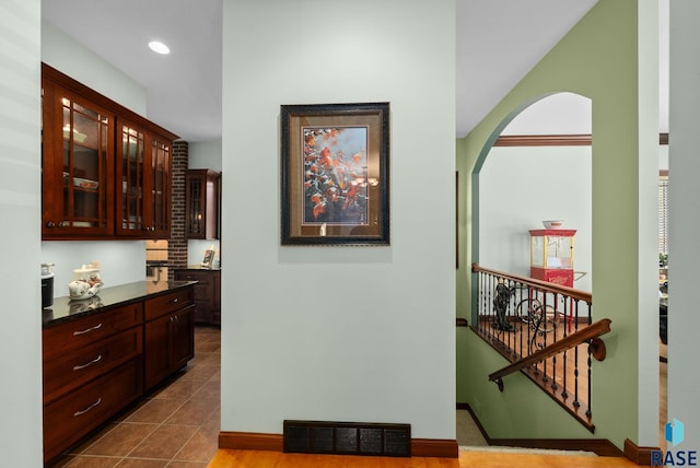 hallway featuring arched walkways, dark tile patterned flooring, baseboards, and recessed lighting