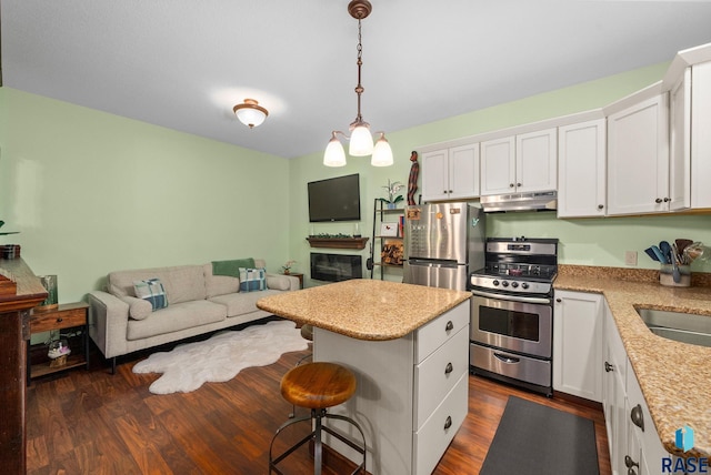 kitchen with stainless steel appliances, under cabinet range hood, white cabinets, and open floor plan