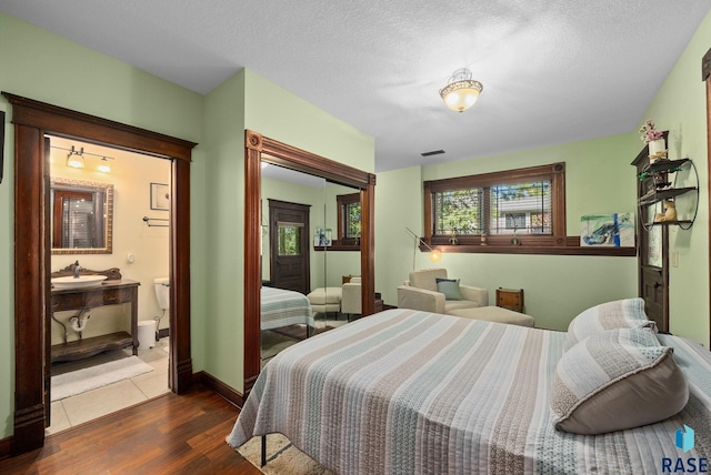 bedroom with dark wood-type flooring, a sink, a textured ceiling, baseboards, and ensuite bathroom