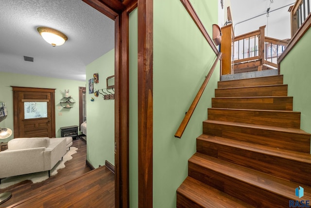 stairway with wood finished floors, healthy amount of natural light, and a textured ceiling