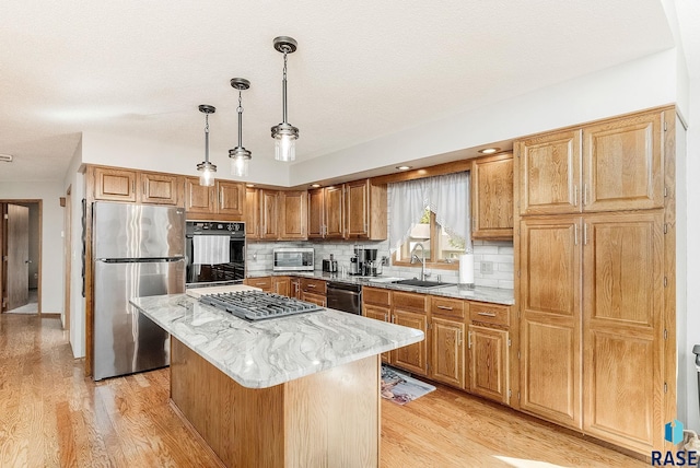 kitchen with black appliances, light wood-style floors, a sink, a center island, and light stone counters